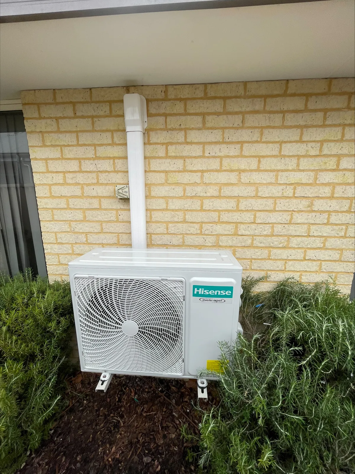 Hisense split system condenser installed on a limestone wall with a neatly run conduit and drain