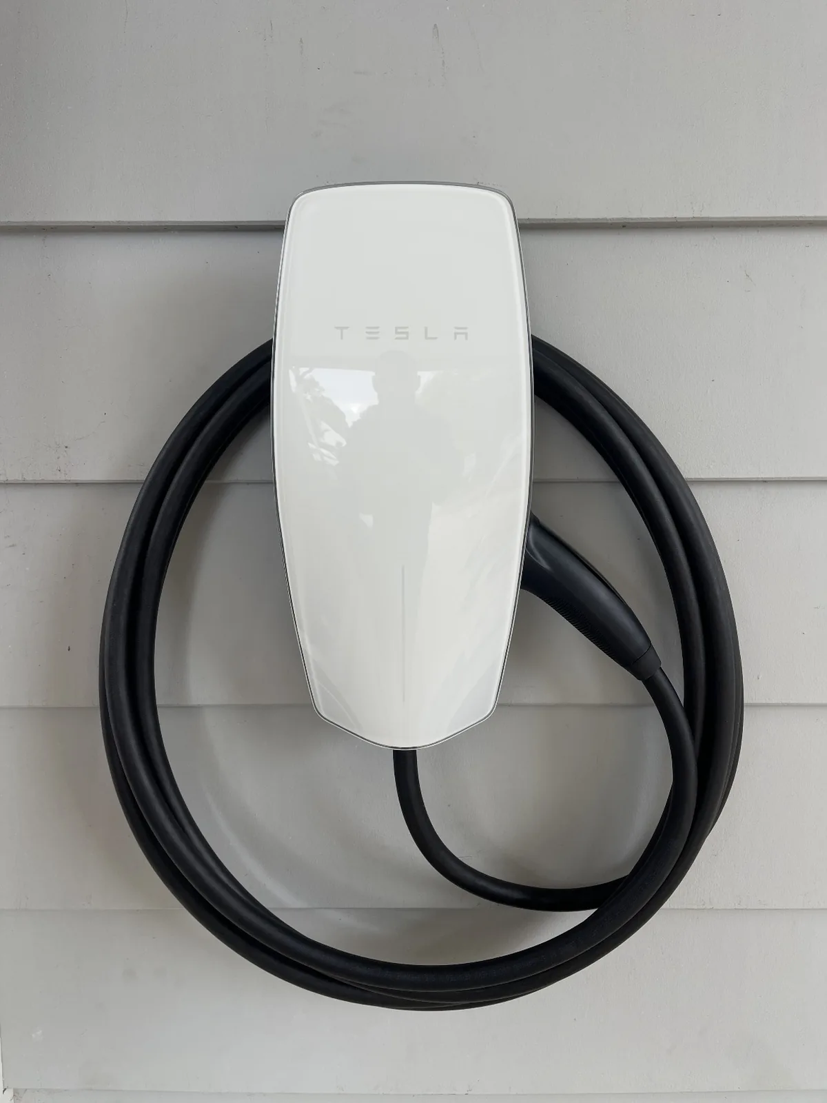 Tesla wall connector and coiled charging lead mounted on the weatherboard wall of a home