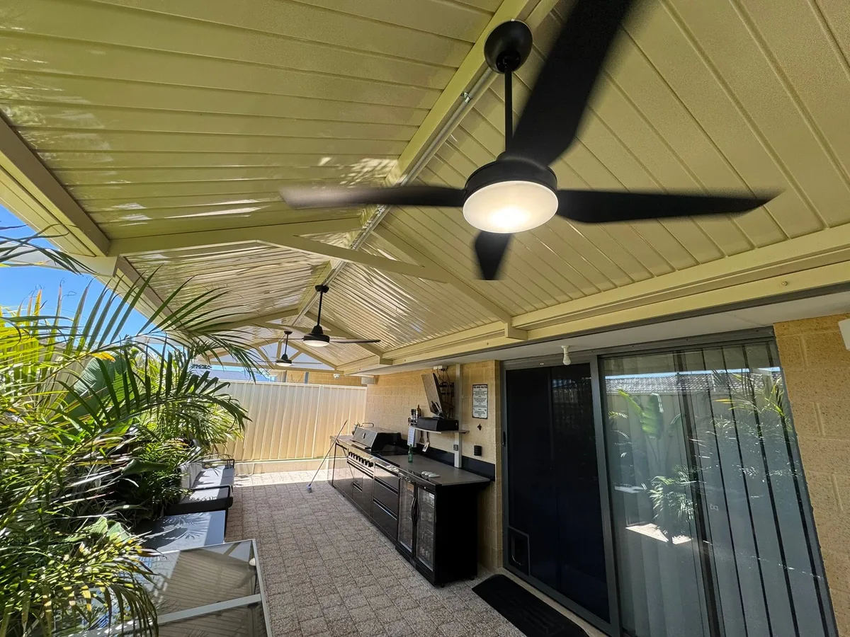 Outdoor kitchen and alfresco living area under a lined patio roof with a ceiling fan