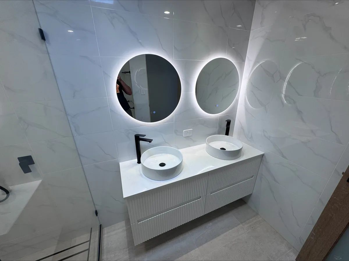 Marble bathroom with a fluted vanity, twin vessel basins, matte black tapware and round backlit mirrors